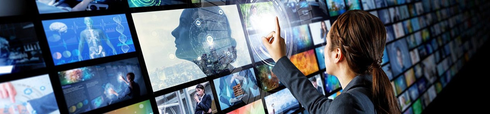 Woman stands in front of a videowall and points at a screen with her finger
